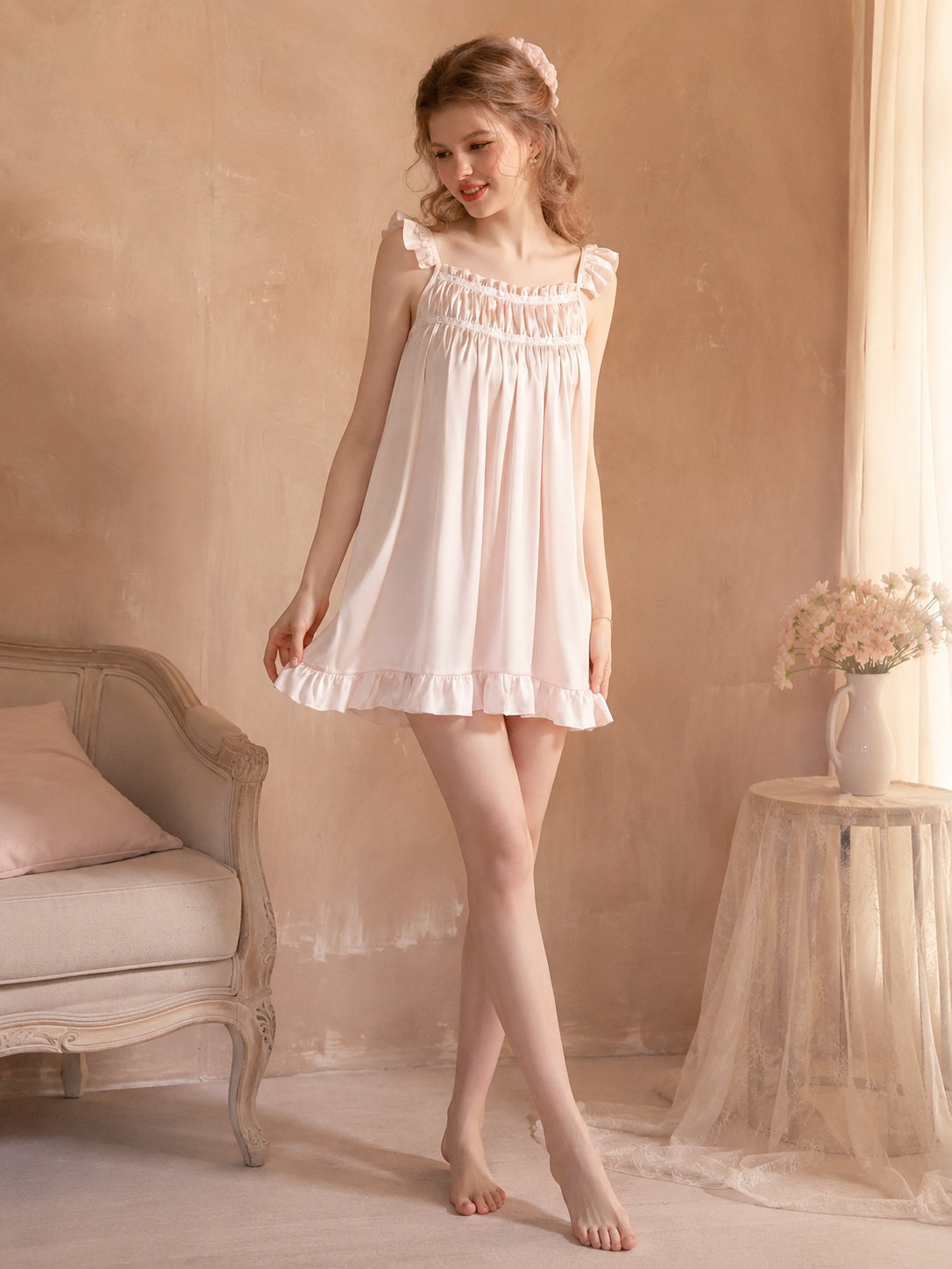 Model wearing blush pink satin ruffle strap sleep dress in soft bedroom setting