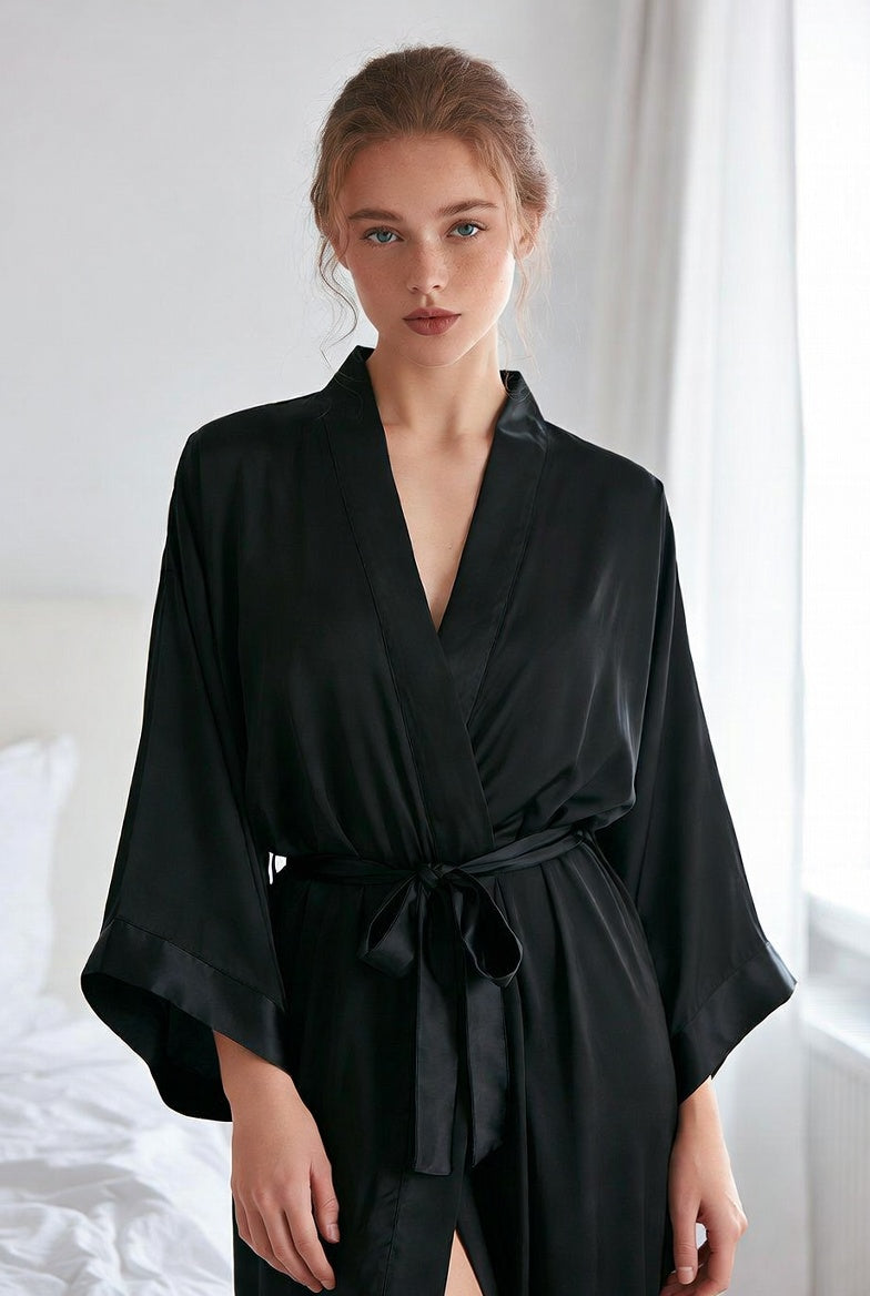 Woman wearing a black silk-like satin kimono robe with wide sleeves and tie waist